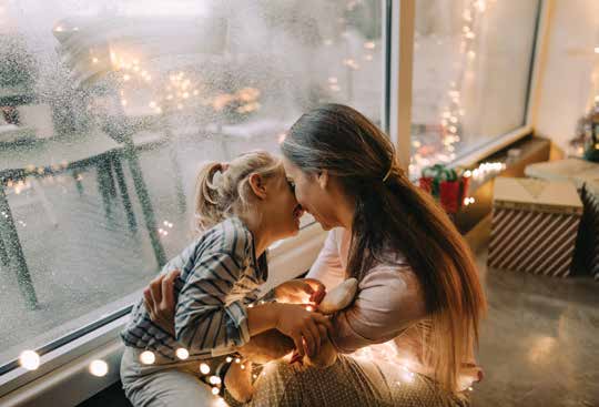 Woman hugging girl with lights wrapped around them.